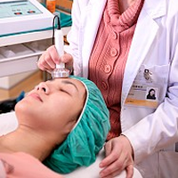 Eine Ärztin vollzieht eine Mikrodermabrasion auf dem Gesicht einer Patientin, sodass mit dem Ultraschall Enzyme eingebracht werden können.